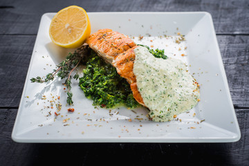 Delicious fish steak with sauce and herbs on wooden background