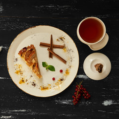 Apple pie with cinnamon on white ceramic wooden plate and cup of hot black tea standing on blue aged wooden surface. Top view.