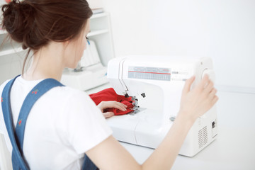Happy attractive young woman seamstress sitting and sews on sewing machine in studio