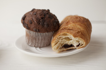 Muffins and croissant for breakfast on white wooden table, top view