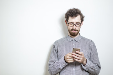 A cool young man uses a smartphone on a white background. Hipster with a beard is writing a message in his mobile phone. Copy space.