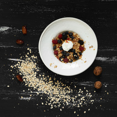 Cereal served with blueberries, blackberries, raspberries, cherries and whipped cream in plate standing on blue old wooden table with ground oats, walnuts and date fruits scattered around. Top view.