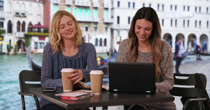 Close-up of couple friends looking at travel map and using laptop computer to locate destination in Venice, Italy, Two beautiful girlfriends using laptop pc with map by Venetian canal, 4k
