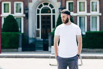 Fototapeta na wymiar Hipster handsome male model with beard wearing white blank t-shirt with space for your logo or design in casual urban style