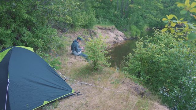 A freelancer man touch a tablet near the forest river and tents.