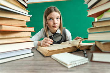 Unhappy teenage girl with magnifying glass surrounded by lots of books / photo of teen school girl, creative concept with Back to school theme