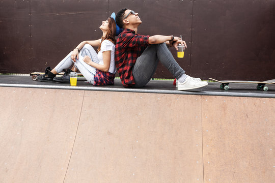 Couple of teenagers skaters sitting on ramp and hangout at the skate park .Laughing and fun.