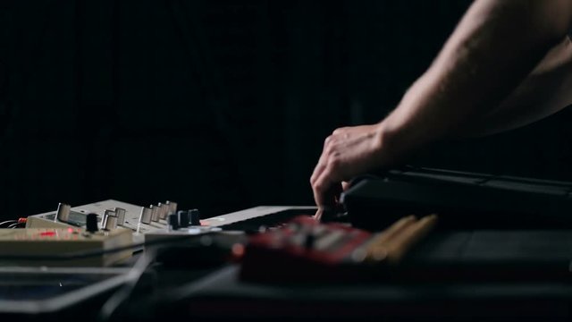 Close up shot of musician's hands play keys and tunes synthesizer
