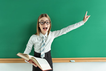 Cheerful enthusiastic pupil with open book pointing finger up. Photo of teen school girl wearing glasses, creative concept with Back to school theme