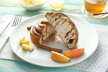 Plate with cut cinnamon bun and fruits on table