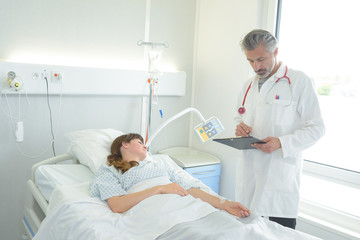 doctor with clipboard standing near patient lying on bed