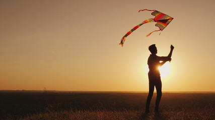 A teenager launches a kite at sunset.
