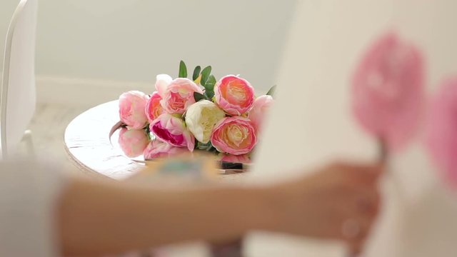 Close-up view of the flowers of the peonies that the girl draws, in the foreground the artist's blurred hand. Flowers in focus.