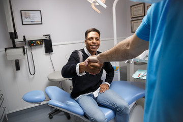 Fototapeta na wymiar Young African-American man shaking hand of crop dentist having visit in medical clinic. 
