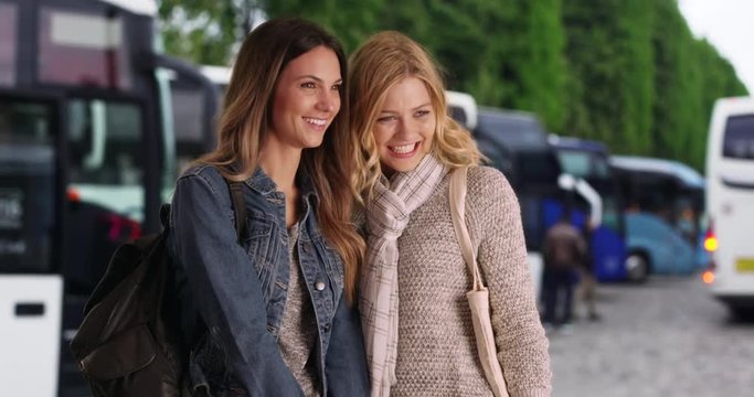 Attractive brunette with blonde female friend chatting together near some tour buses, Couple of pretty young female tourists gossiping in Paris, France, 4k