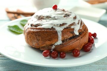 Plate with glazed cinnamon bun and cranberries on table