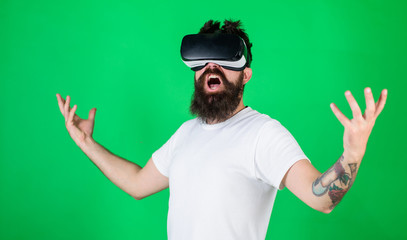 Man with beard in VR glasses, green background. Power concept. Hipster on shouting face raising hands powerfully while interact in virtual reality. Guy with head mounted display interact in VR