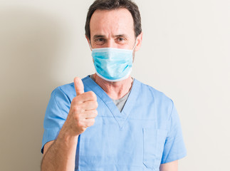 Senior doctor man using mask happy with big smile doing ok sign, thumb up with fingers, excellent sign