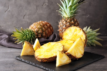 Slate plate with delicious cut pineapples on table - obrazy, fototapety, plakaty