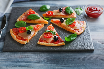 Slate plate with slices of delicious pizza on wooden table