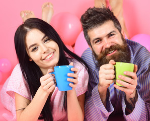 Couple in love drink coffee in bed. Couple relax in morning with coffee. Family tradition concept. Man and woman in domestic clothes, pajamas. Man and woman on smiling faces lay, pink background.