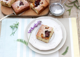 Pieces of fruit pie with pieces of plums and peach and a bouquet of flowers on a wooden table. Rustic style.