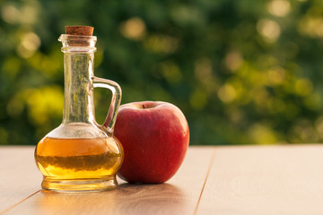 Apple vinegar in glass bottle and fresh red apple on wooden boards with green natural background