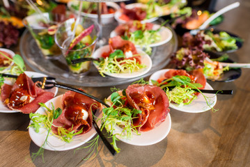 Tasty little snacks with meat and vegetables on served table at the restaurant