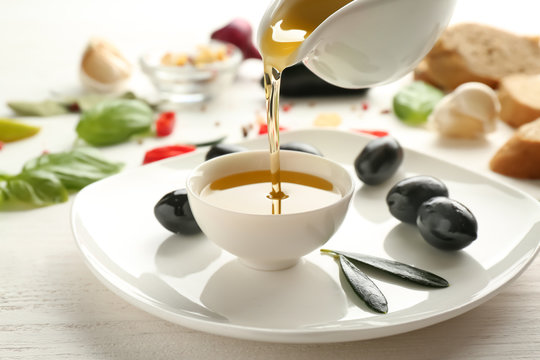 Pouring of olive oil from jug into bowl on table