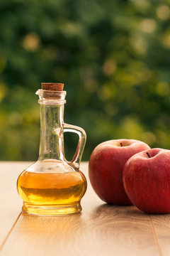 Apple vinegar in glass bottle and fresh red apple on wooden boards with green natural background