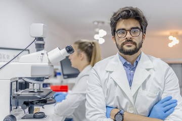 Closeup portrait, young friendly scientist standing by microscope. Isolated lab background....