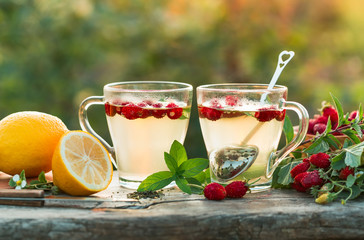Two cups of hot tea with strawberry and mint on a old table in the open air.