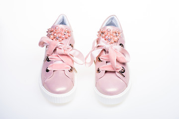 Glamorous sneakers concept. Pair of pale pink female sneakers with velvet ribbons. Cute shoes isolated on white background. Footwear for girls and women decorated with pearl beads.