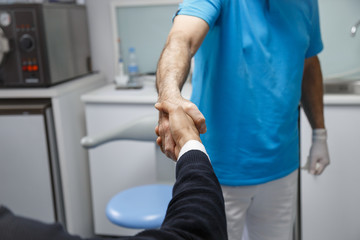 Young African-American man shaking hand of crop dentist having visit in medical clinic. 