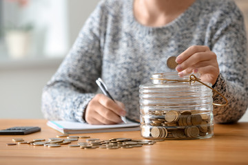 Woman putting coins into glass jar on table. Savings concept