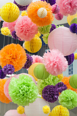 Bright decorations of paper colored POM-poms. POM-poms made of paper hanging from the ceiling. Background of colored spots.