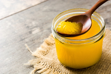 Ghee or clarified butter in jar and wooden spoon on wooden table. Copyspace