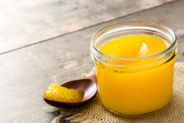 Ghee or clarified butter in jar and wooden spoon on wooden table. Copyspace