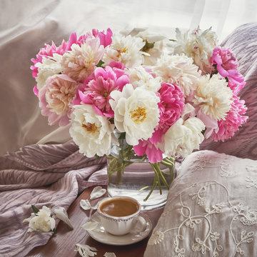 Colorful peony flowers bouquet in glass vase, cup of coffee. Toned image