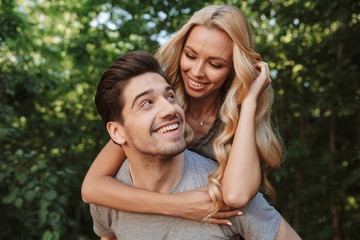 Fototapeta premium Smiling young man carrying his pretty girlfriend on his back