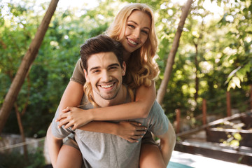 Fototapeta premium Happy young man carrying his pretty girlfriend on his back
