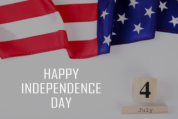 Ruffled American flag and wooden cube calendar with 4th of July congratulations. Happy Independence Day greeting card text on grey copy space background. Top view, close up, vintage toned filter.