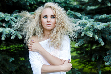 Photo of curly long-haired woman next to fir branches