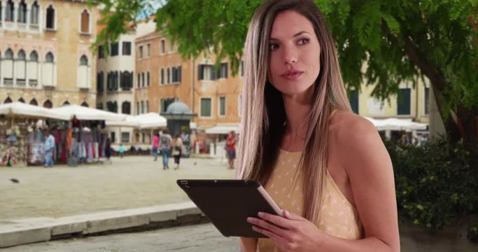 Happy white woman using tablet computer and smiling outside in Italian city setting, Friendly Caucasian girl in her 20s using pad device in street in Venice, Italy, 4k