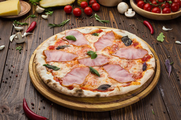 Delicious italian pizza with ham and basil leaves on wooden background