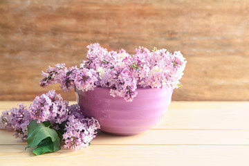 Bowl with beautiful blossoming lilac on table against wooden background