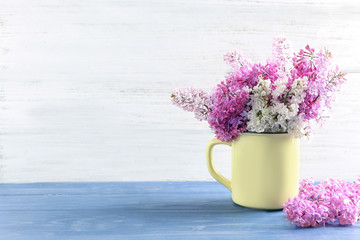 Cup with beautiful blossoming lilac on table against wooden background