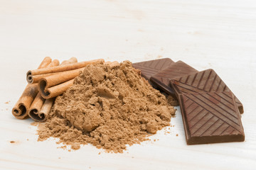Dark chocolate and cinnamon sticks and powder on wooden background