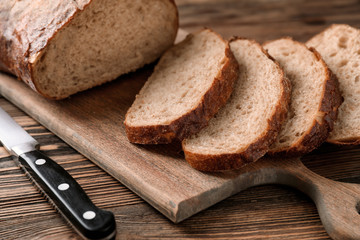 Knife and board with cut fresh tasty bread on wooden table