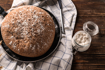 Frying pan with tasty fresh bread and jar of flour on wooden table